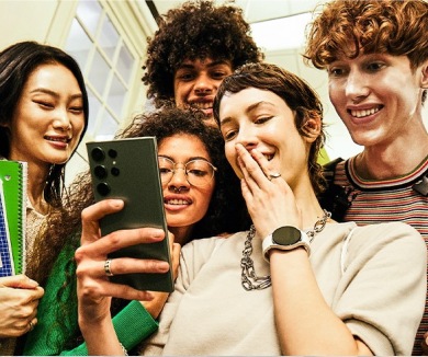 Группа друзей, сидя снаружи, смеясь и глядя на свои смартфоны. Там показаны значок Galaxy Store и другие значки.