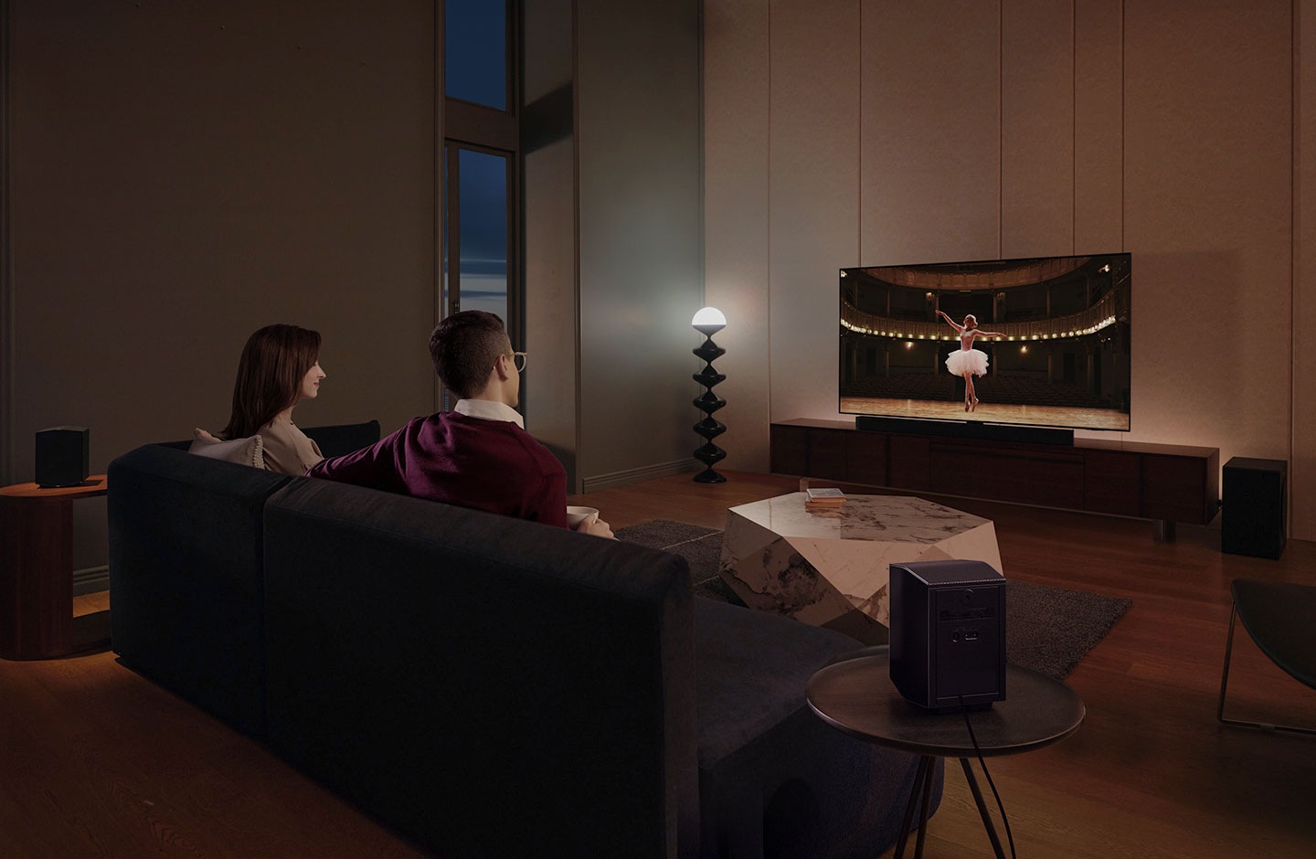 زوجان يستمتعان بمشاهدة فيلم السهرة في غرفة معيشتهما من خلال الصوت المحيطي الأشبه بصوت السينما الذي يتميز به جهاز الصوت من Samsung.