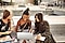 A group of three cheerful female students sitting on a bench in front of a Samsung Galaxy Book2 Pro 360.