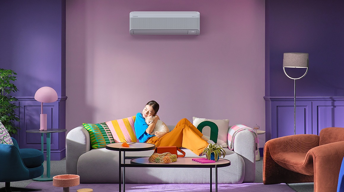 A young girl hugs a cat as she relaxes on a couch. Behind her is a wall-mounted WindFree AC.