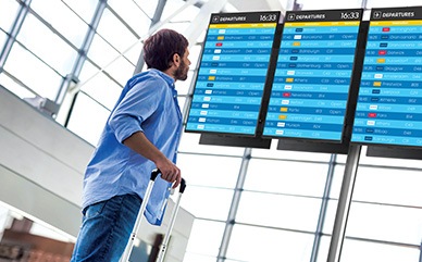 A man at the airport is checking the flight information displayed on the QxB screen.