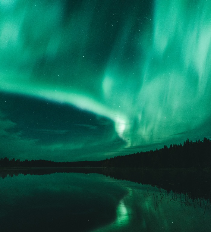 Nattvy över norrsken över en sjö som reflekterar ljuset.