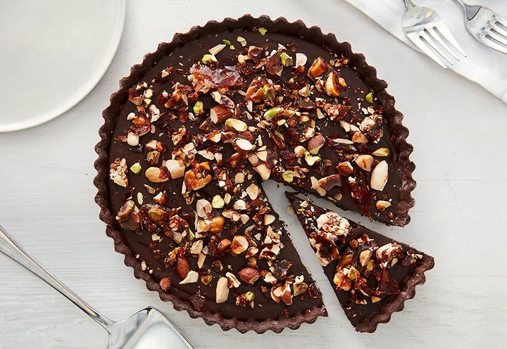 Chocolate tart topped with mashed nuts on it is on a white table.