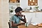 A man sits at a table in his kitchen, using a light grey Galaxy Book Pro laptop. He is also wearing a pair of black Galaxy Buds Pro in his ears.