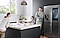 A mother and daughter eat salad with orange juice in the kitchen, while the father watches over them and smiles while standing next to the Family Hub, where the screen display indicates rainy weather and reads "Good Morning Chris."