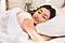 A woman smiling with her head on a pillow in bed.
