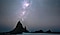 A beach rock formation in front of a starry night sky.
