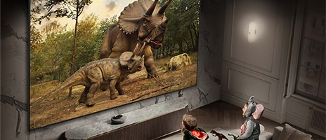Two youngsters donning animal costumes are engrossed in watching two dinosaurs on Samsung's expansive Supersize display in the living room.