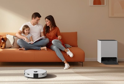 A family sits on a couch using a tablet while a robot vacuum, a Samsung Jet Bot Combo, cleans the floor and an air purifier stands nearby in a living room.