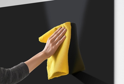 A hand using a yellow microfiber cloth to clean a Samsung TV screen, emphasizing proper screen care.