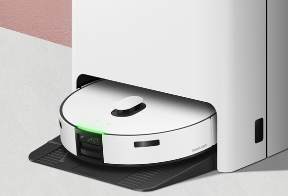 A Samsung Jet Bot Combo robot vacuum docked in its white charging station with a green LED light indicating it is charging.