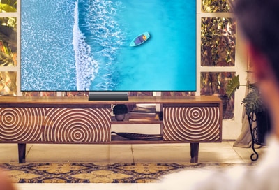 A person viewing a 2025 Samsung Smart TV displaying a vibrant aerial image of a boat on blue water.