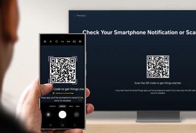 Person holding a phone with a QR code on the screen, aimed at a Samsung Smart TV displaying a similar QR code for setup.