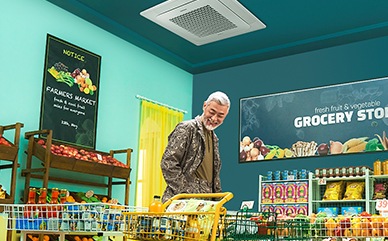 A man pushes a cart filled with groceries under a 4-way cassette in a grocery store.
