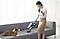 The woman cleans the sofa with a jet 75. There is a dog on the left.