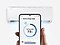 In front of a air conditioner, a hand holds a Galaxy smartphone displaying the AI energy mode SmartThings app UI.