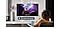 Kanepenin üzerinde oturan bir kadın, aydınlık bir oturma odasının duvarına monte Smart TV’sinde konser videosu izliyor. Kadın elinde tuttuğu Smart TV uzaktan kumandasına “Sesi kıs” diyerek sesli asistanı etkinleştiriyor.