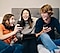 Троє друзів, сидячи на дивані зі своїми смартфонами, сміються та діляться інформацією про ексклюзивні ігри в Galaxy Store .