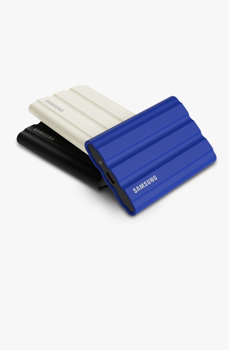 Показано три Portable SSD T7 Shield. Чорний і бежевий портативні SSD-накопичувачі лежать вертикально один на одному. Портативний SSD-накопичувач синього кольору лежить під горизонтальним кутом перед двома іншими SSD-накопичувачами.