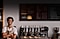 A barista stands smiling with arms crossed in front of a coffee machine and a menu board inside a coffee shop.