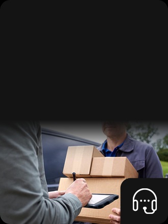 An individual holds a Samsung device and writes on it with an S Pen. In the background someone carries boxes