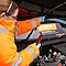 A woman looking under a bonnet with a phone in a her hand