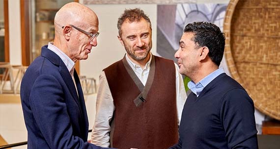 An image of two men shaking hands whilst another man is watching. All 3 men are partaking in a conversation.