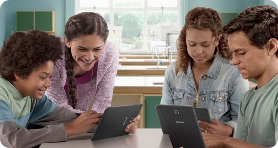 Two young people are engaged with a tablet, while two others are using their own devices in the background.