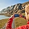 A man taking a picture of scenery using a smartphone.
