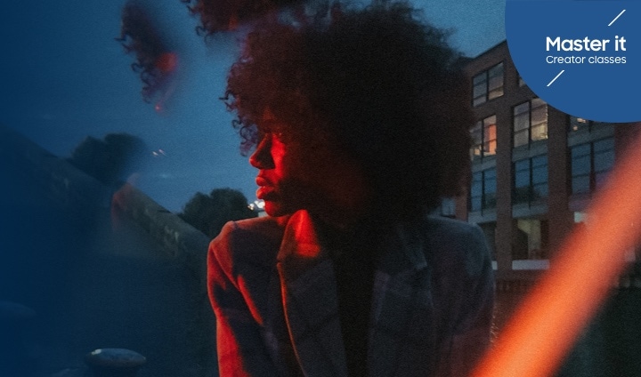 A woman in a jacket looking to the left, subtly illuminated by a red light in front of a blue sky. Master it Creator classes.