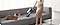 A woman using Samsung cordless adjustable handheld vacuum cleaner to clean a couch with a dog sitting nearby