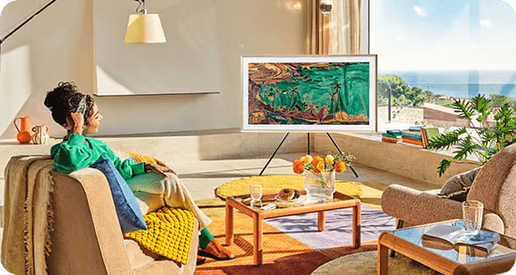 A woman watches a TV with a Studio Stand. The TV displays a painting in horizontal mode.