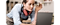 A woman is folded over a Samsung laptop, starring at the screen. She is holding a pencil and wearing a apron and headphones round her neck.
