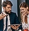 Two people in smart clothes look down at a Samsung tablet. The female is smiling