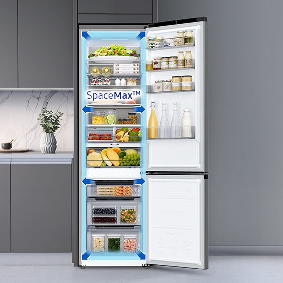 Ușa unui frigider este deschisă pentru a prezenta interiorul său SpaceMax. Frigiderul este plin cu alimente și băuturi, aranjate pe rafturi și sertare.
