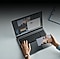 A person watches a video on a laptop while holding a phone in their right hand.
