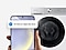 In front of a washing machine, a hand holds a Galaxy smartphone displaying the SmartThings app UI with drum clean notification.