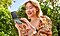 A female in a floral blouse is shown in a park setting with a Galaxy Z Flip5 open in her hand.