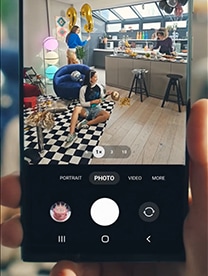 A female sits on a black and white checked carpet blowing up balloons. Around her is a bar area and party decorations. This is to show off Samsung’s camera graphics.
