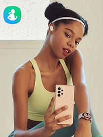A female in sportswear poses in front of a background, holding her phone as though she is taking a selfie, to show Samsung’s Health apps.