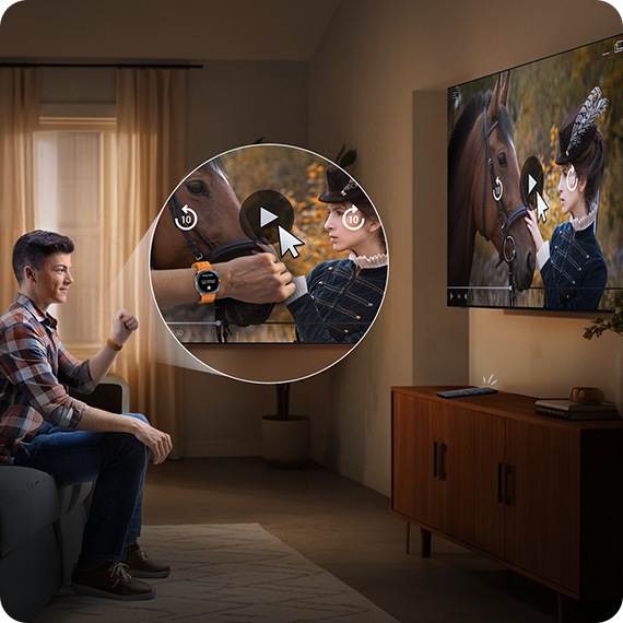 Man wearing a Galaxy Watch watches TV in a living room. He moves his hand back and forth to play the video on the screen with Universal Gestures.
