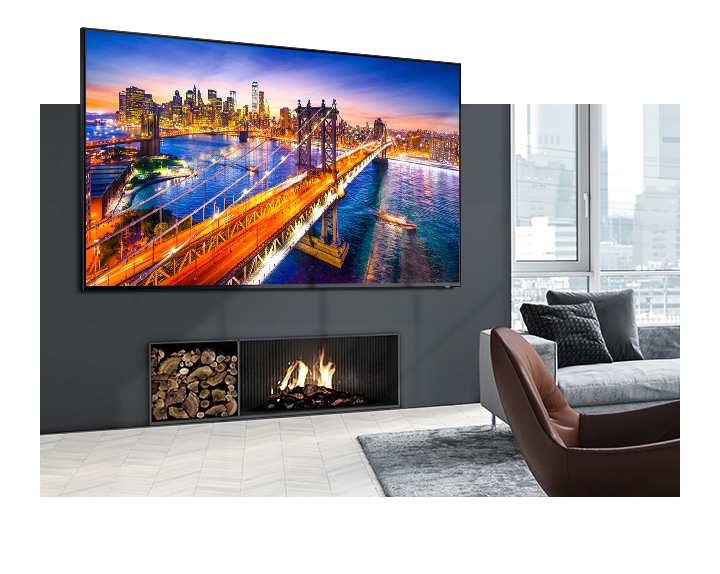 A wall mounted TV over a fireplace displays a bridge night scene with a city in clear picture quality by Dynamic Mode of Samsung picture settings in the bright and cozy living room.