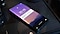 A black Galaxy phone lies on a table in a darkened room. The display is lit in purples and pinks, with a silhouette of a mountain range. The time and date appear on the display, along with a SmartThings alert notification. The message 'Baby crying' appears in the notification box.