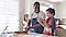 A father wearing a blue apron is baking next to his son who is wearing a red apron. His daughter is on the right side of the father clapping while father and son are making dough on a granite kitchen countertop.