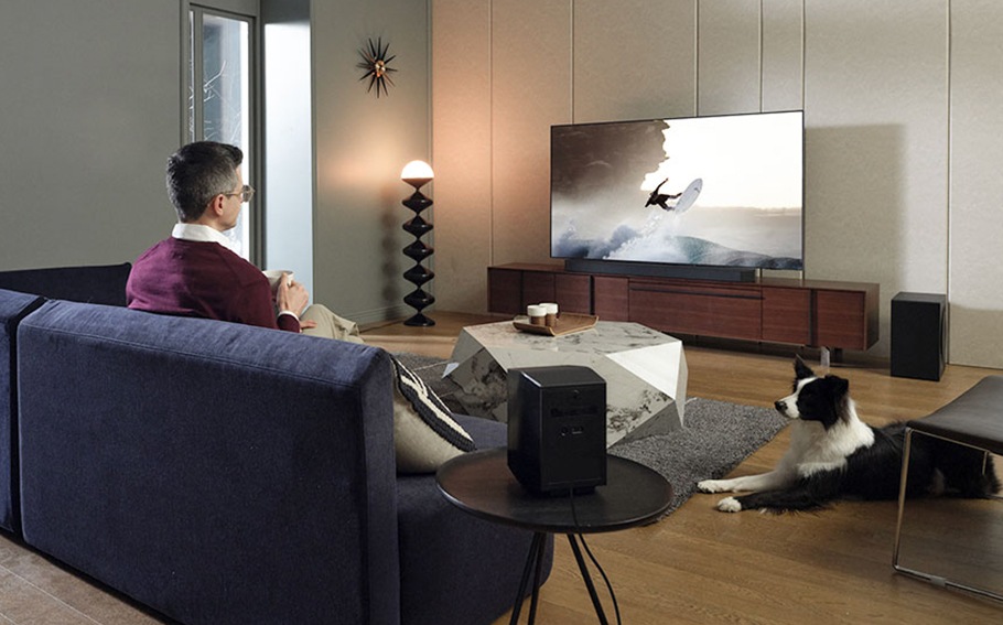 A man is engulfed in the refreshing sounds of the ocean as he watches a surfer on TV.