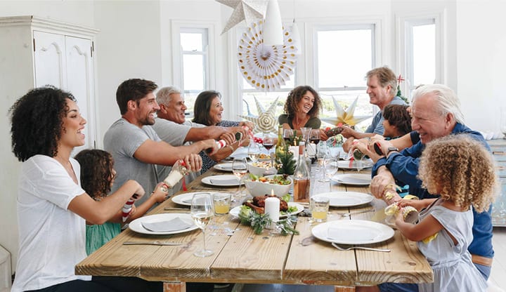 A smiling family sits around a dining room table getting ready to pull Christmas crackers