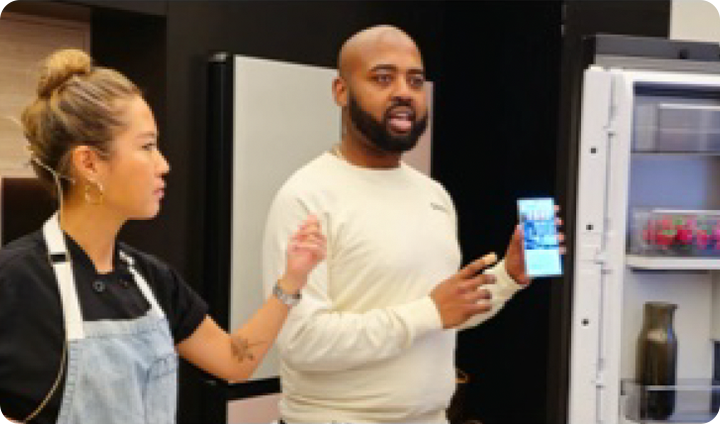 A Samsung ambassador presents to a crowd with a Samsung Galaxy device and a Samsung refrigerator.