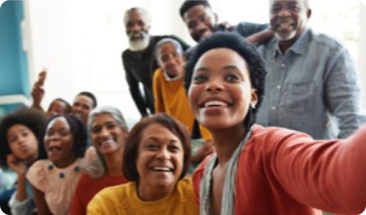 A young woman takes a selfie with her whole extended family smiling in the background