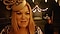 A still from Joe Wright's film, Princess & Peppernose. We see a close-up of a blonde woman wearing a fascinator hat, with a woman singing in the background.