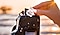 A woman's hand is inserting a memory card into a DSLR camera. A beach and pier in the background.